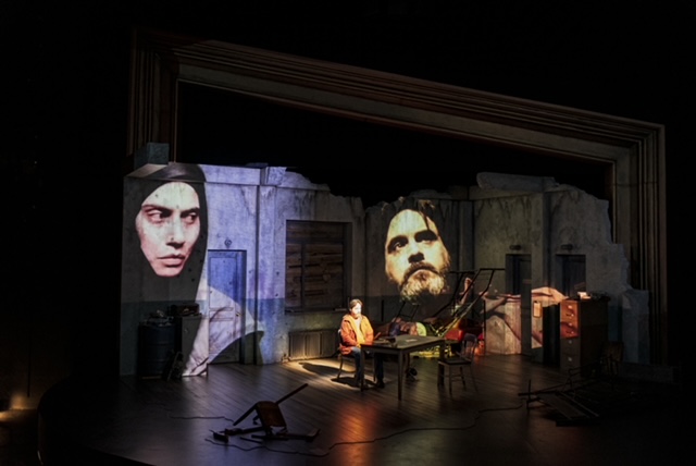 A woman performs on a stage lit with projections. 